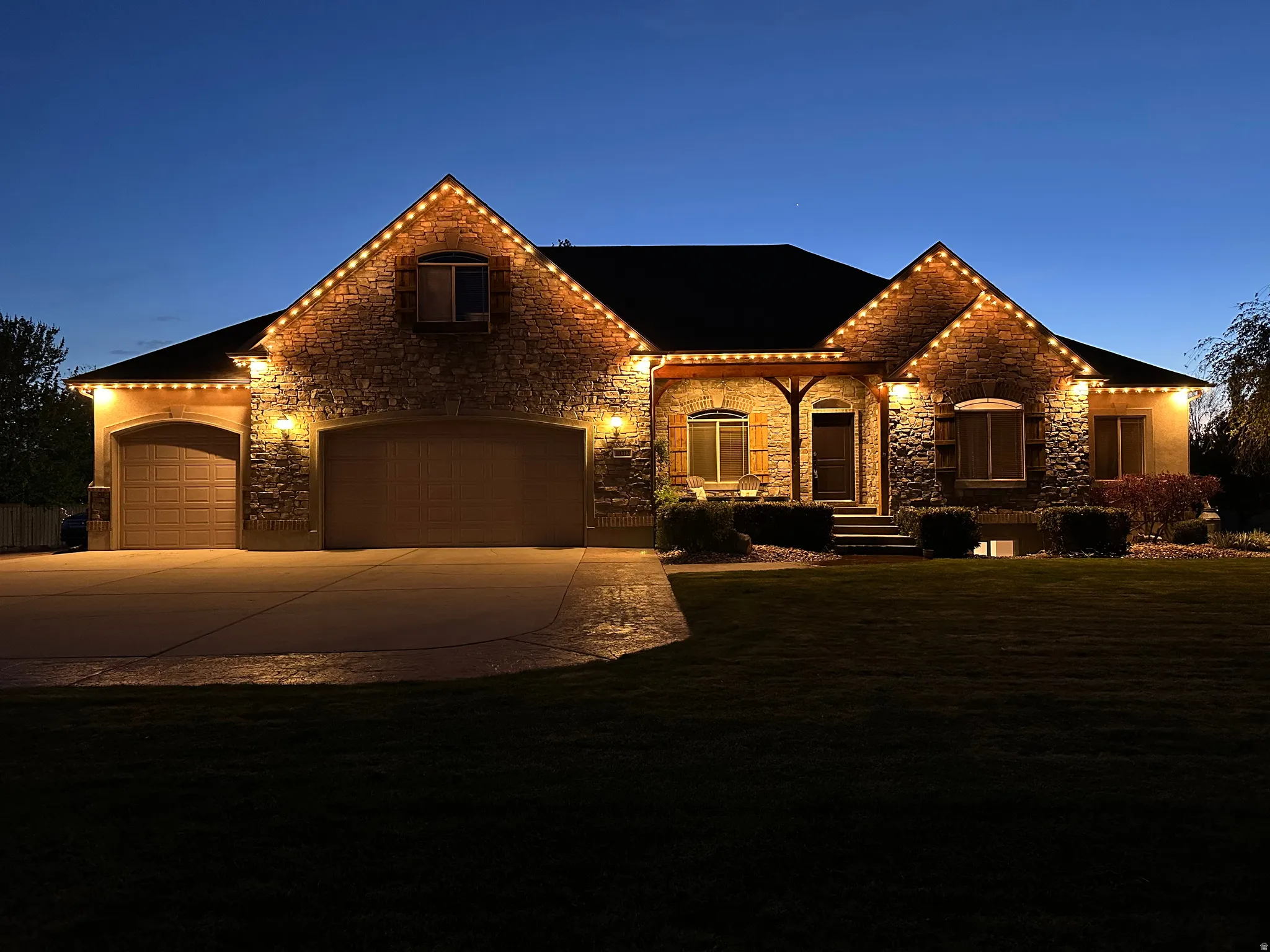 View of front of house with stone siding, an attached garage, driveway, a front lawn, and a shingled roof