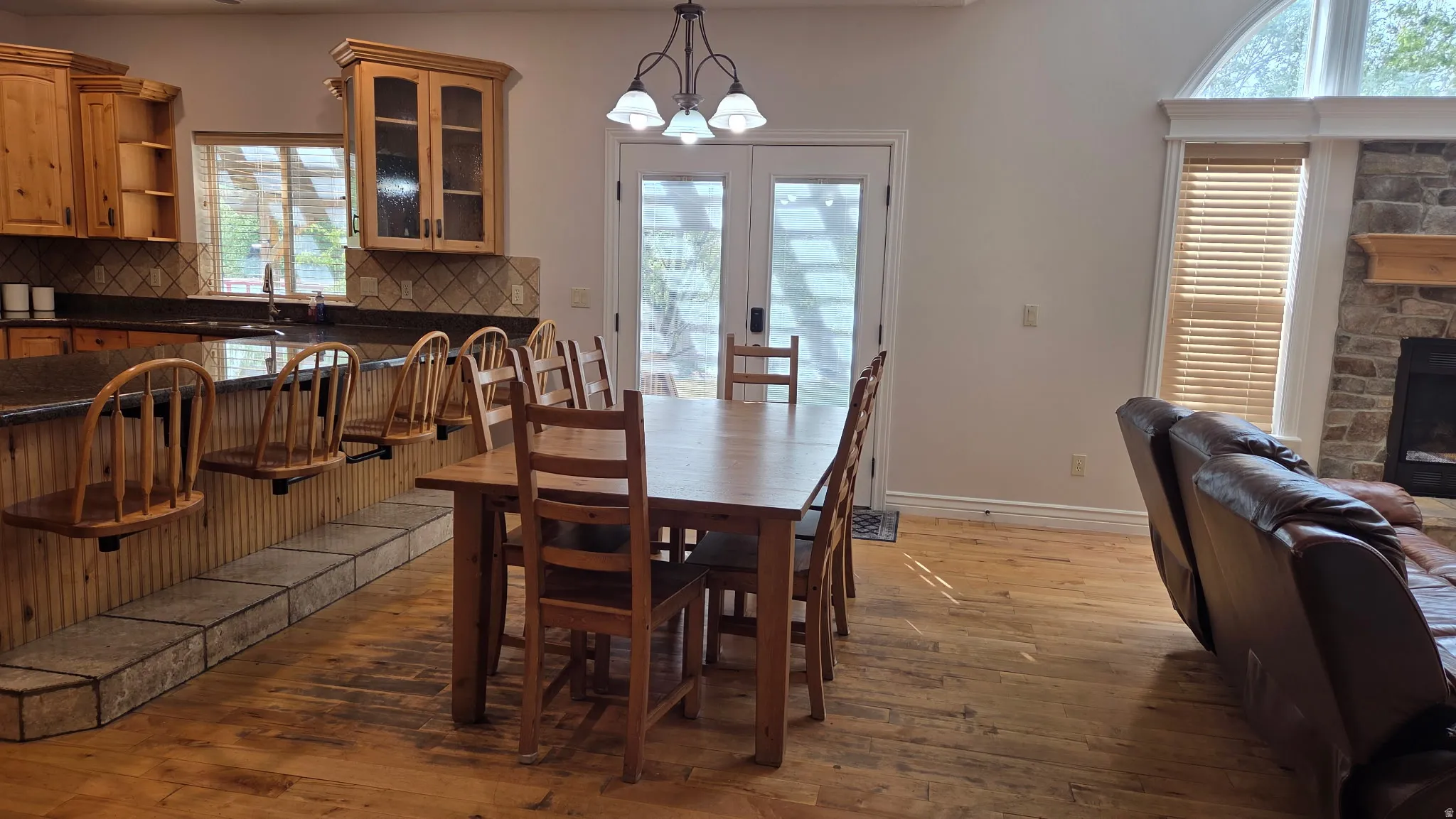 Dining space with light wood-style floors, hanging lights, and a stone fireplace
