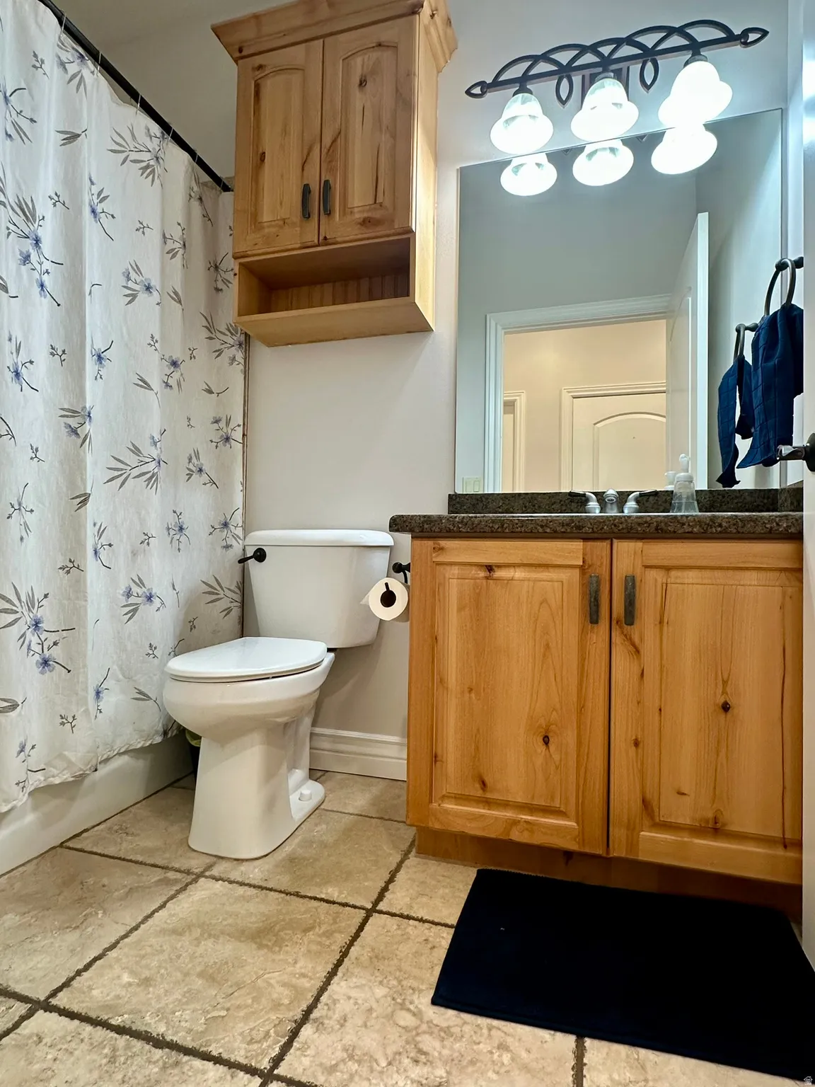 Travertine flooring with a light-toned wood vanity featuring a granite countertop