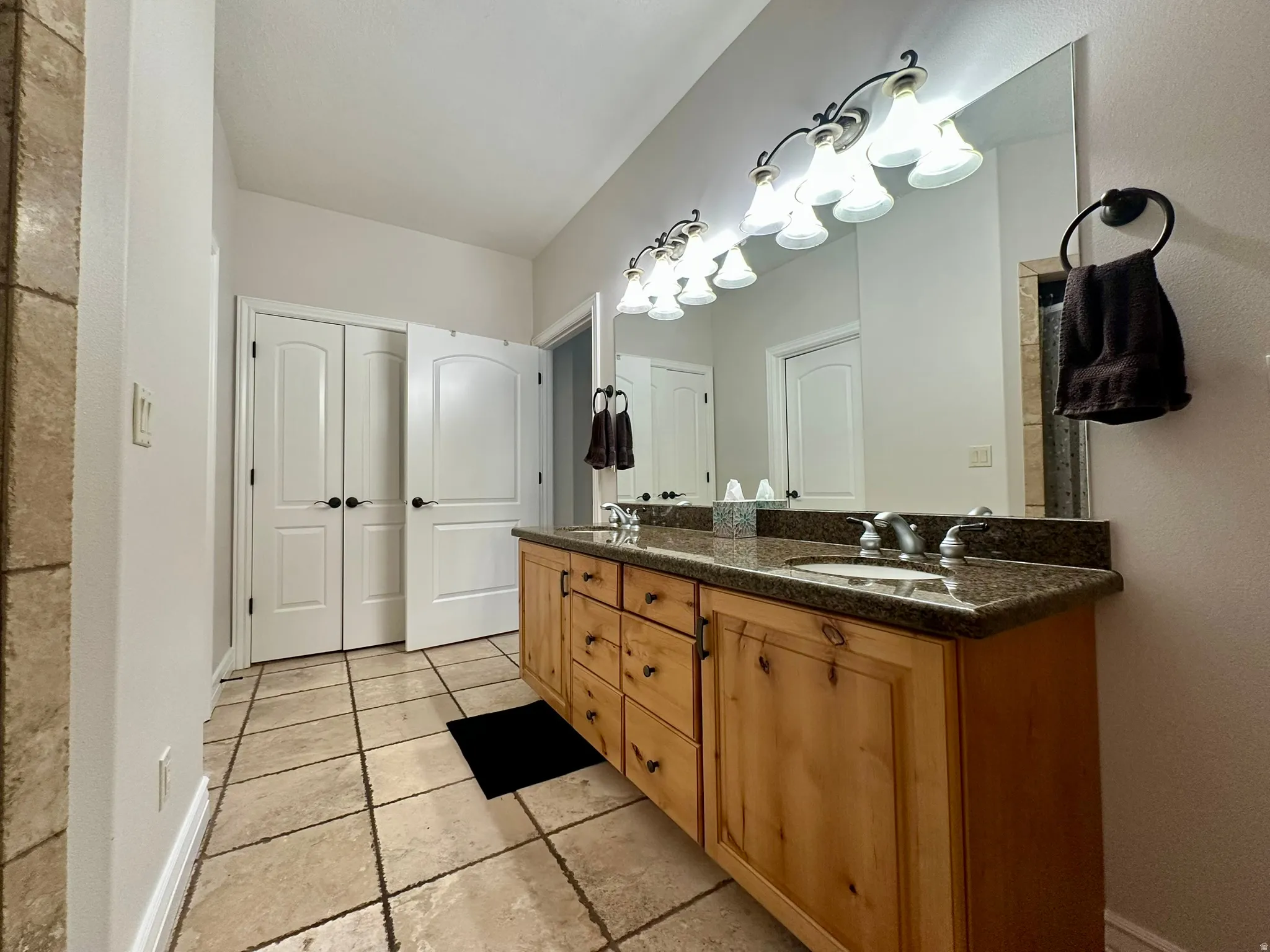 Double vanity featuring a light wood cabinet with dark hardware, a speckled countertop, and two under-mount sinks
