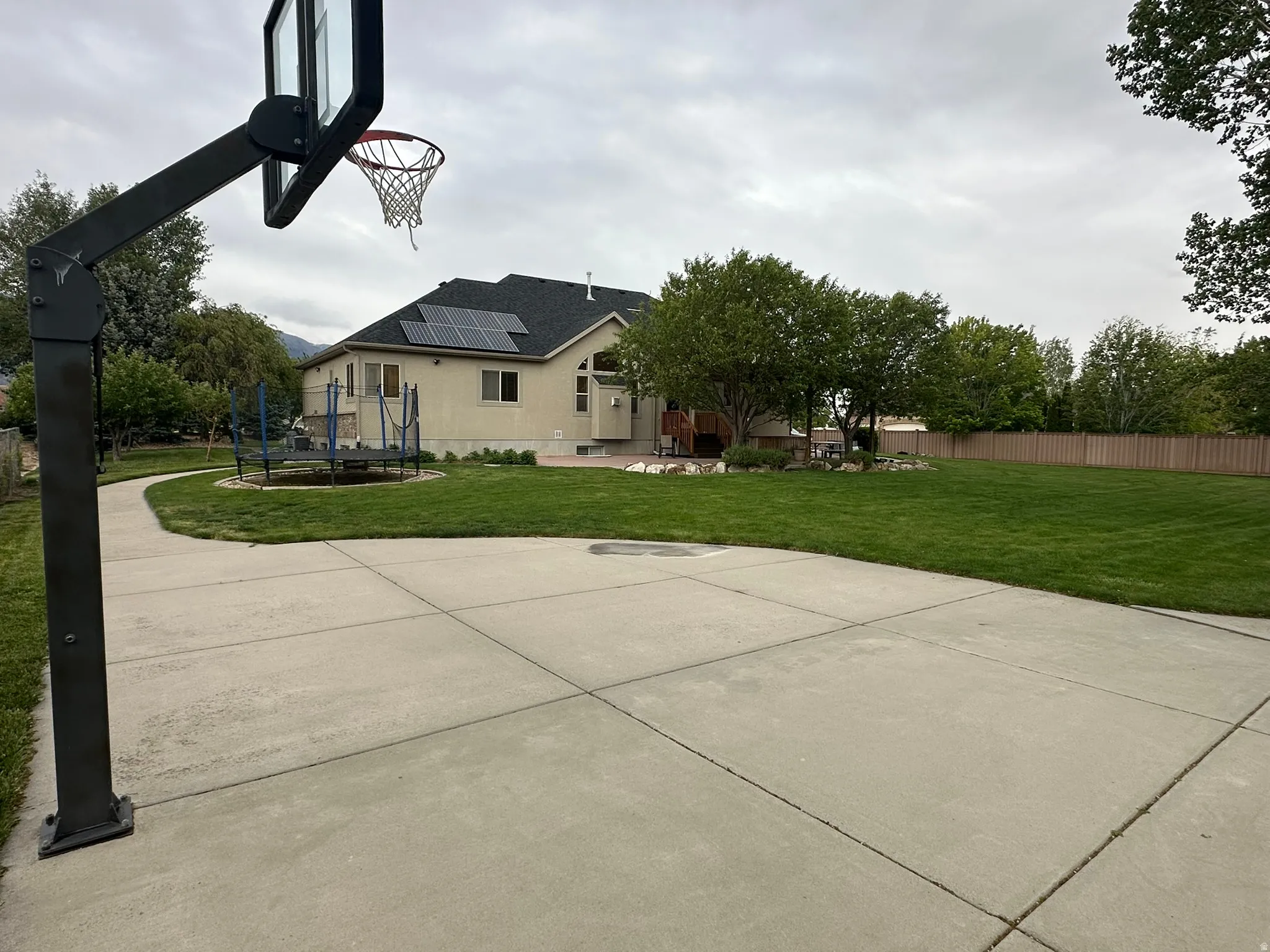 Expansive concrete sports court with an adjustable hoop, complemented by a sprawling lawn.