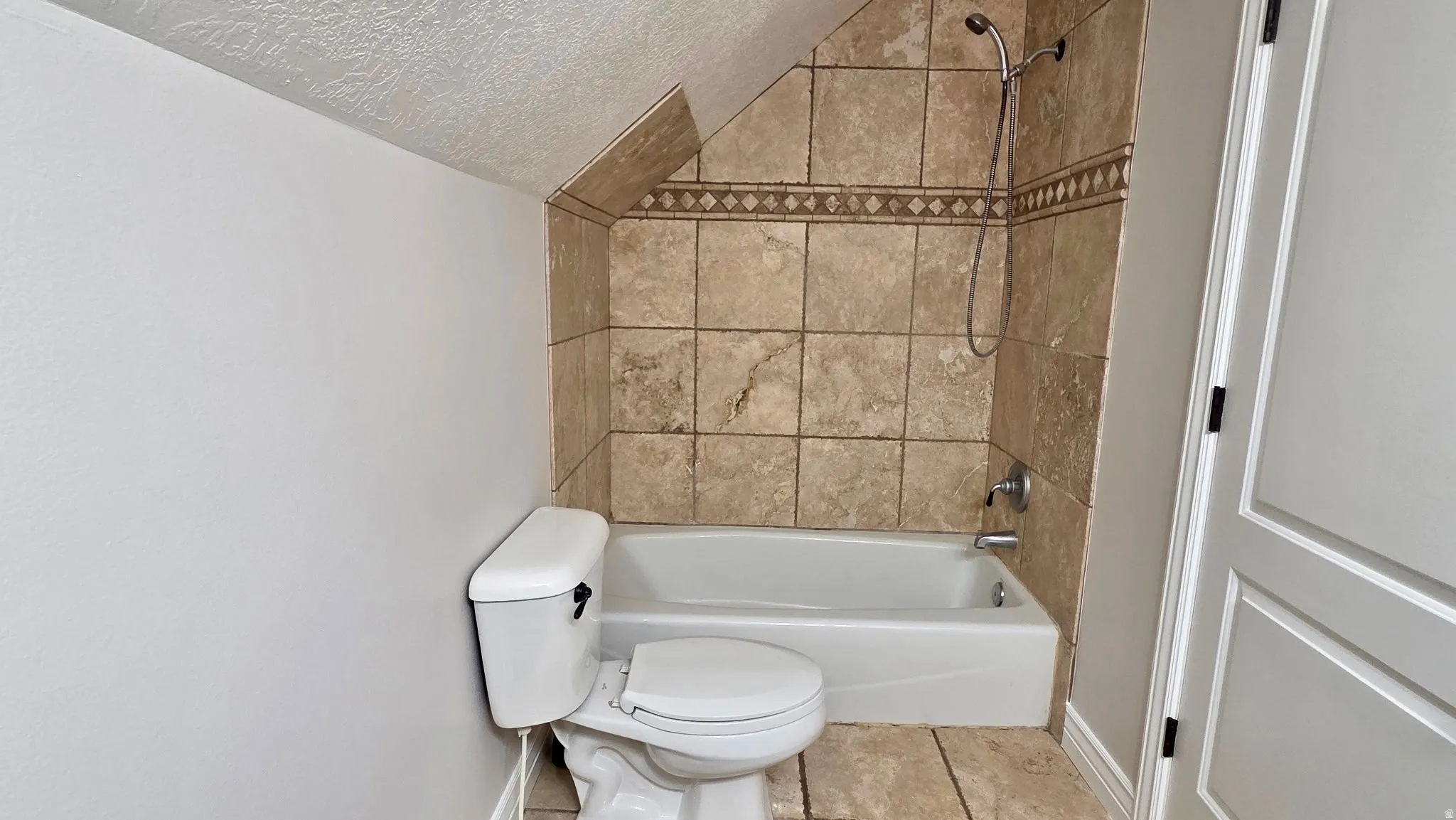 Bathroom featuring shower / bathtub combination, a textured ceiling, and light tile patterned flooring