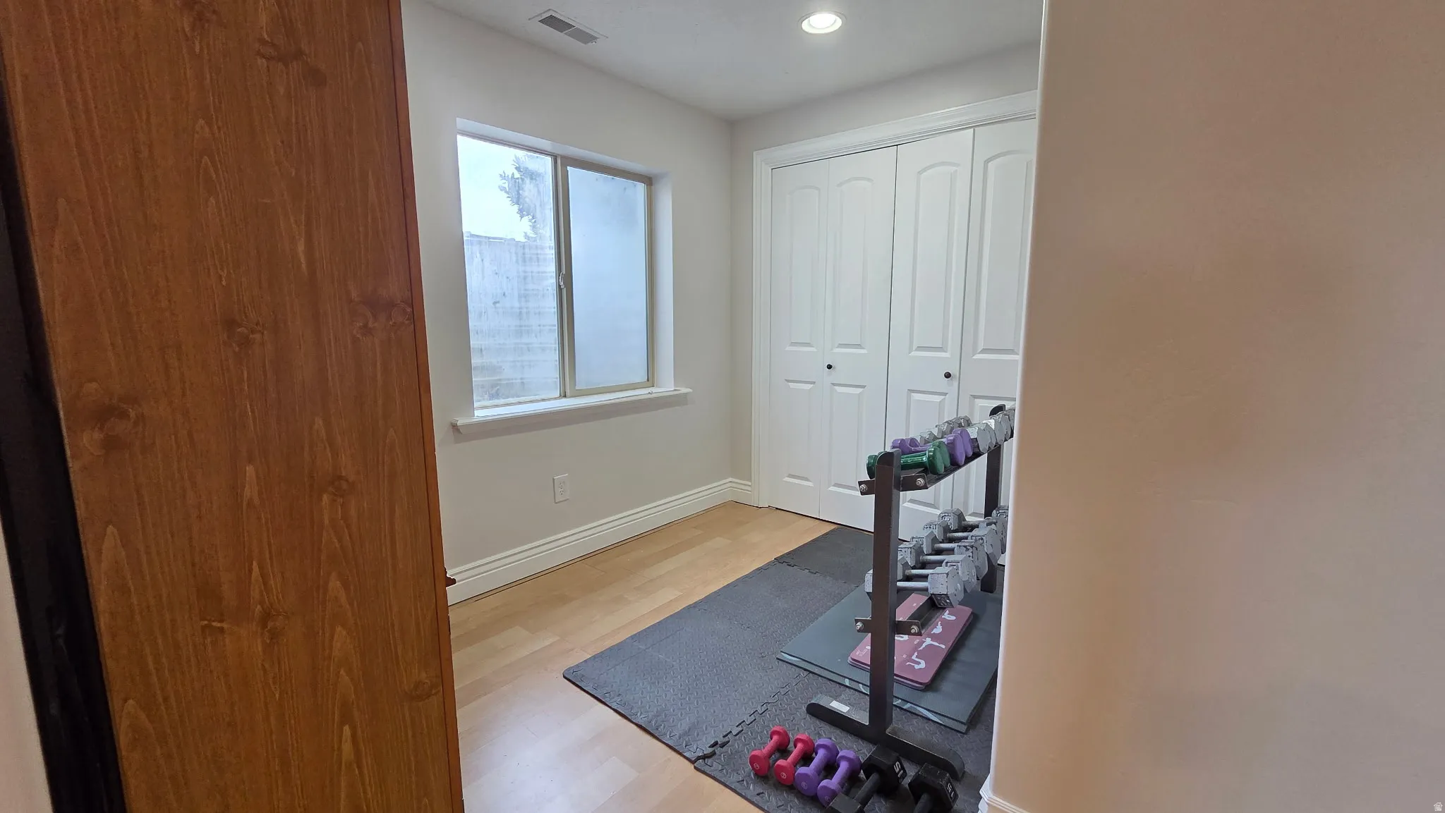 Exercise room with light wood-style floors and recessed lighting