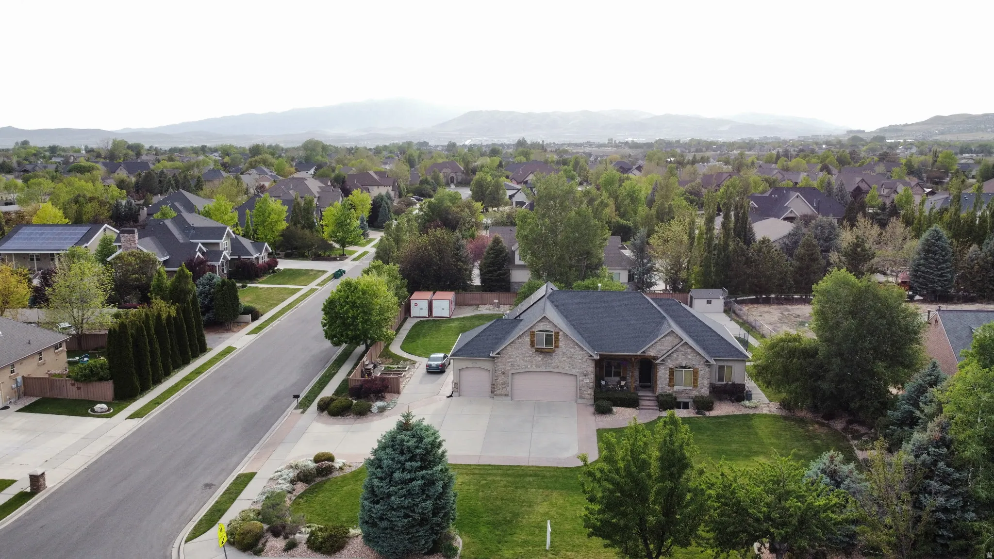 Stone and stucco exterior residence featuring a dark shingle roof, attached garage, and a concrete driveway
