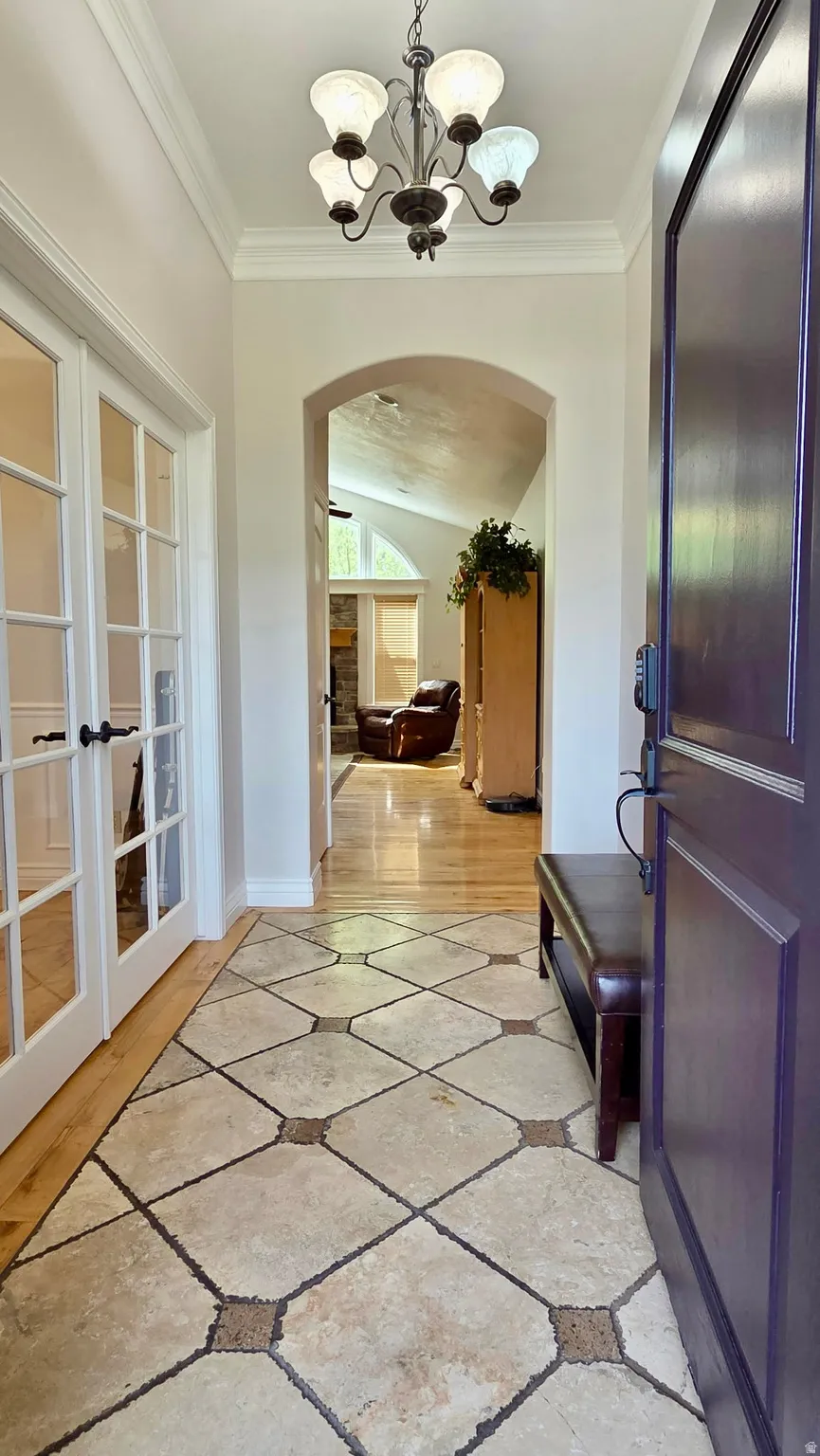 Foyer entrance featuring inlaid floor details, arched walkways, a chandelier, vaulted ceiling, and ornamental molding