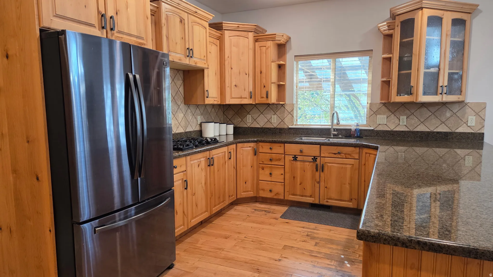 Kitchen with freestanding refrigerator, light wood-style floors, open shelves, and dark stone countertops