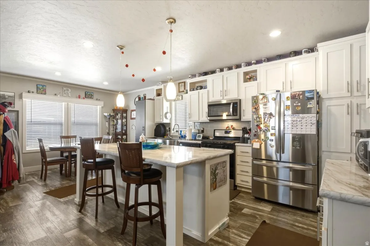 Kitchen featuring stainless steel appliances, a center island, a breakfast bar, white cabinetry, and hanging light fixtures