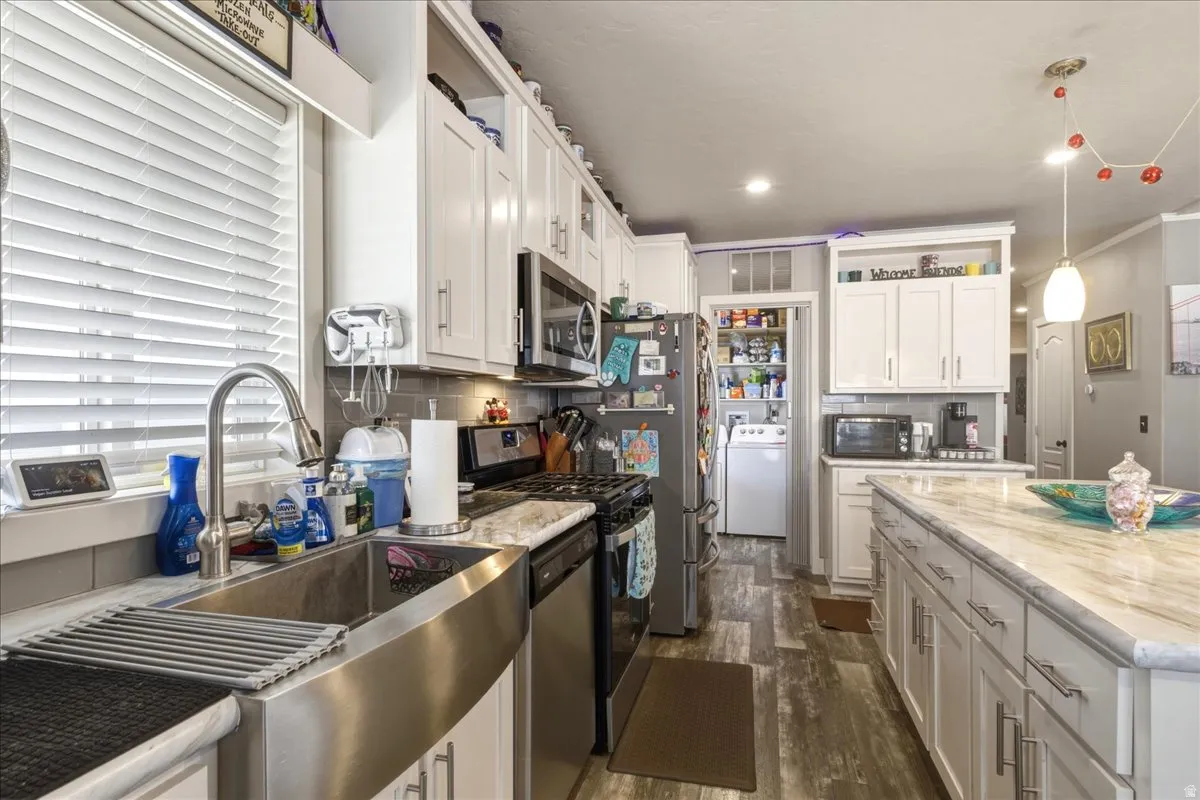 Kitchen featuring white cabinets, washer / dryer, stainless steel appliances, dark wood-style floors, and decorative backsplash