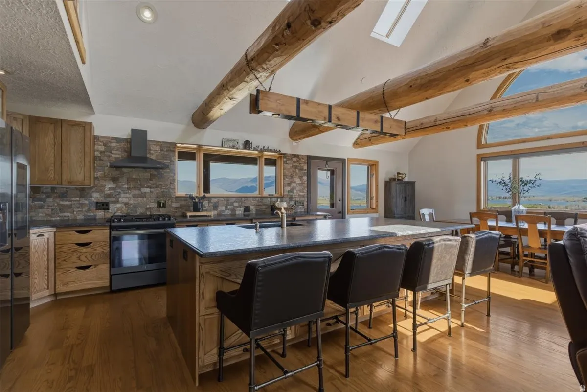 Kitchen featuring a center island with sink, stainless steel appliances, backsplash, wood finish cabinets, and lofted ceiling