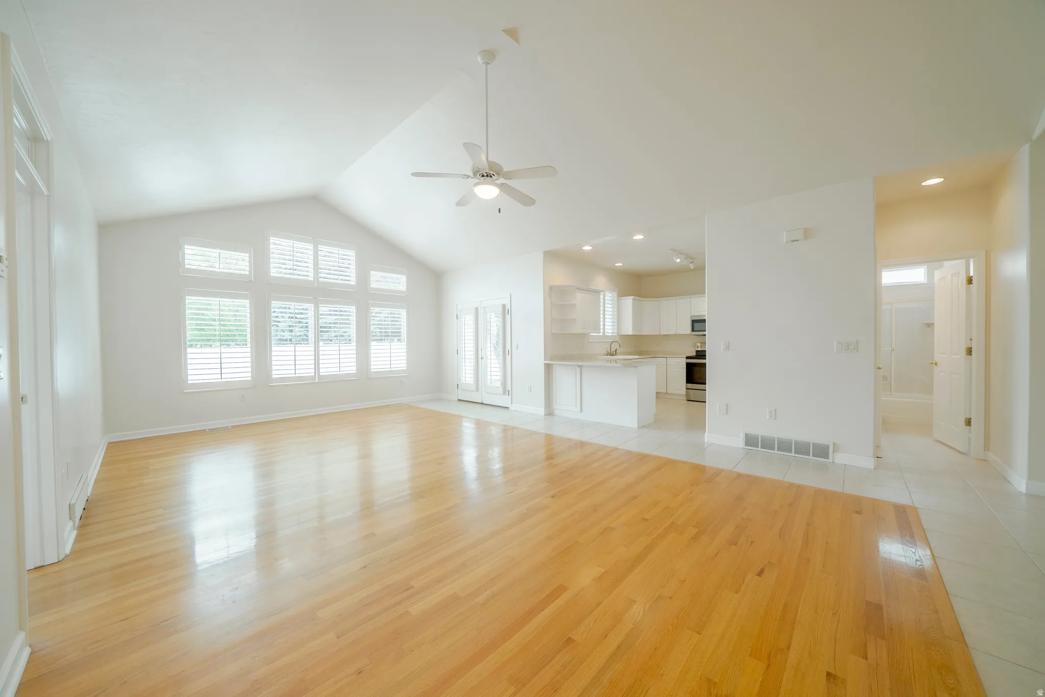 Unfurnished living room featuring light wood-style floors, a ceiling fan, a high ceiling, and recessed lighting