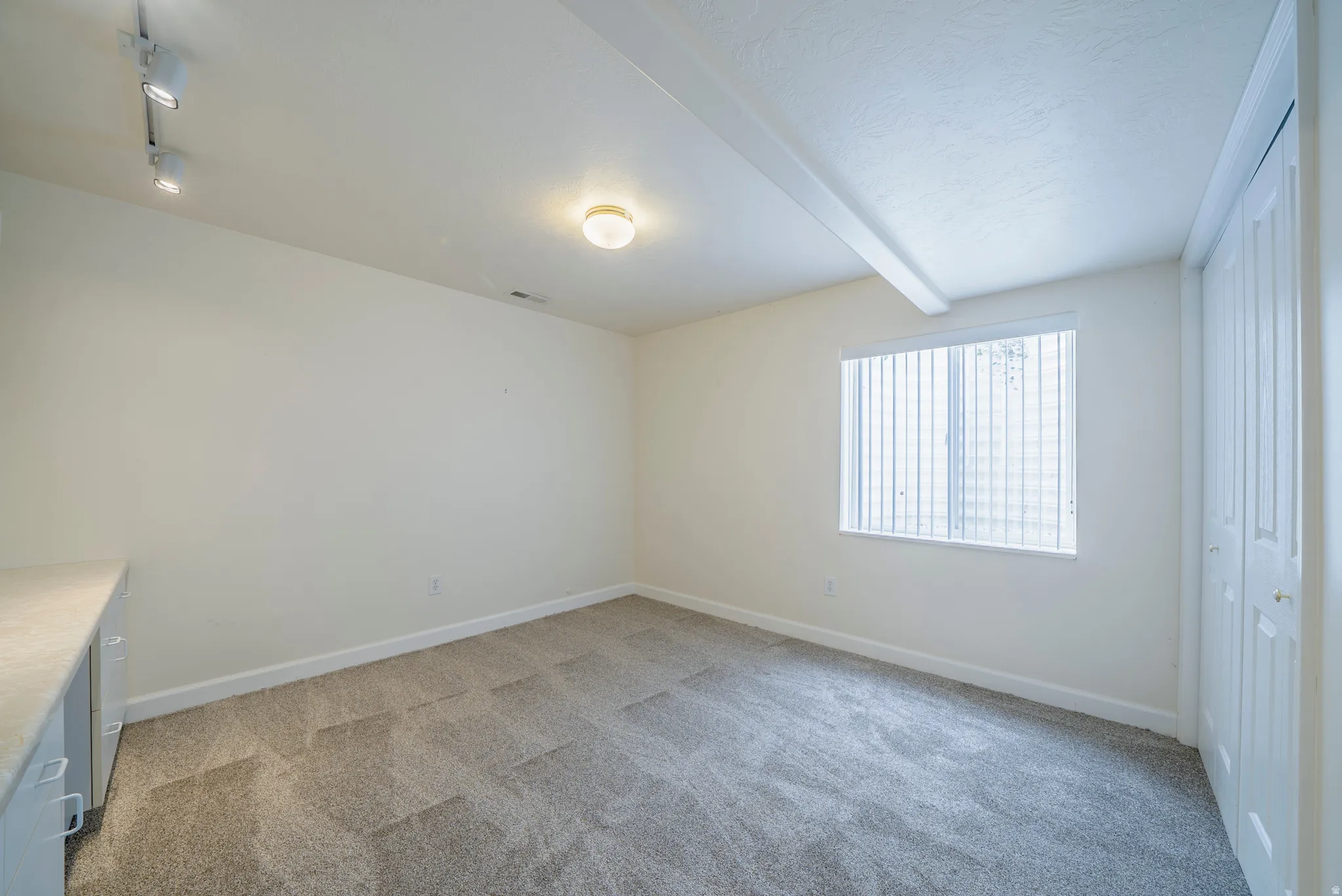 Unfurnished bedroom featuring light colored carpet and track lighting