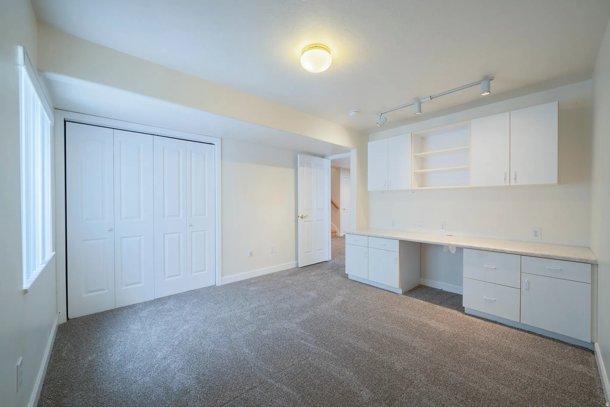 Unfurnished office with built in desk, rail lighting, and dark colored carpet