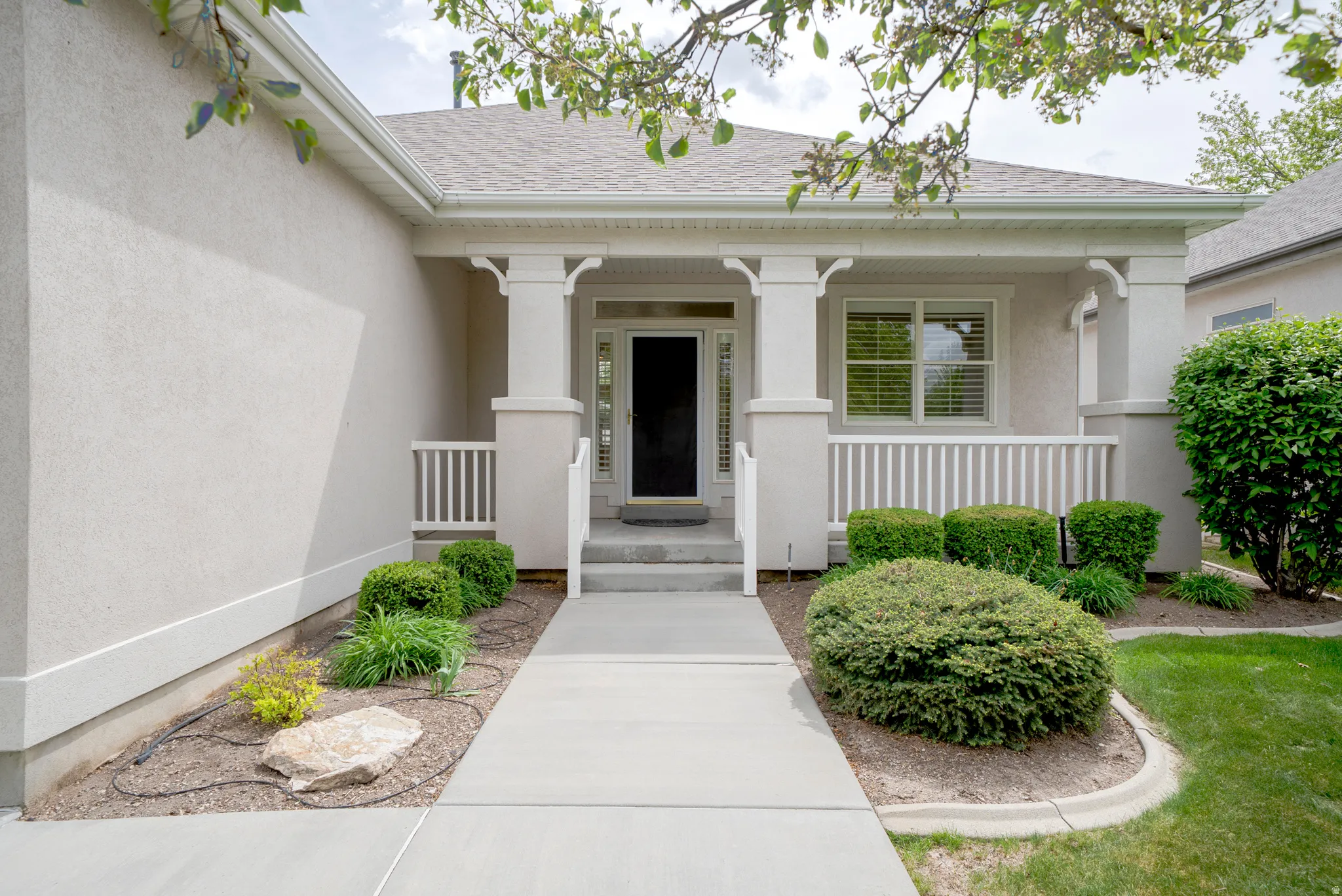 Doorway to property with covered porch, roof with shingles, and stucco siding