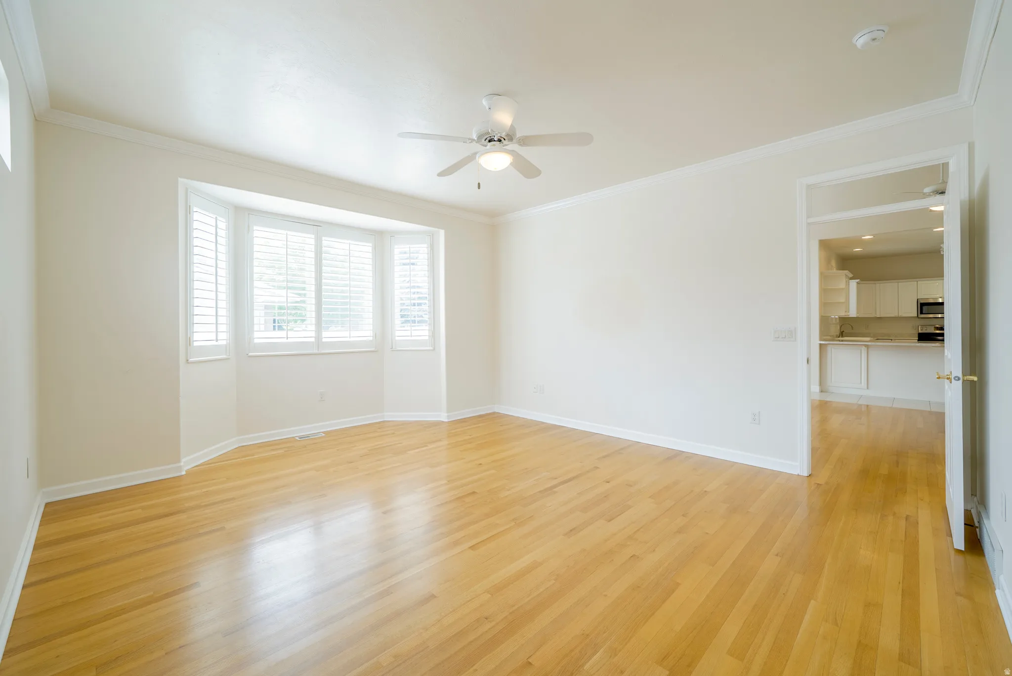Empty room with light wood-type flooring, ornamental molding, and a ceiling fan