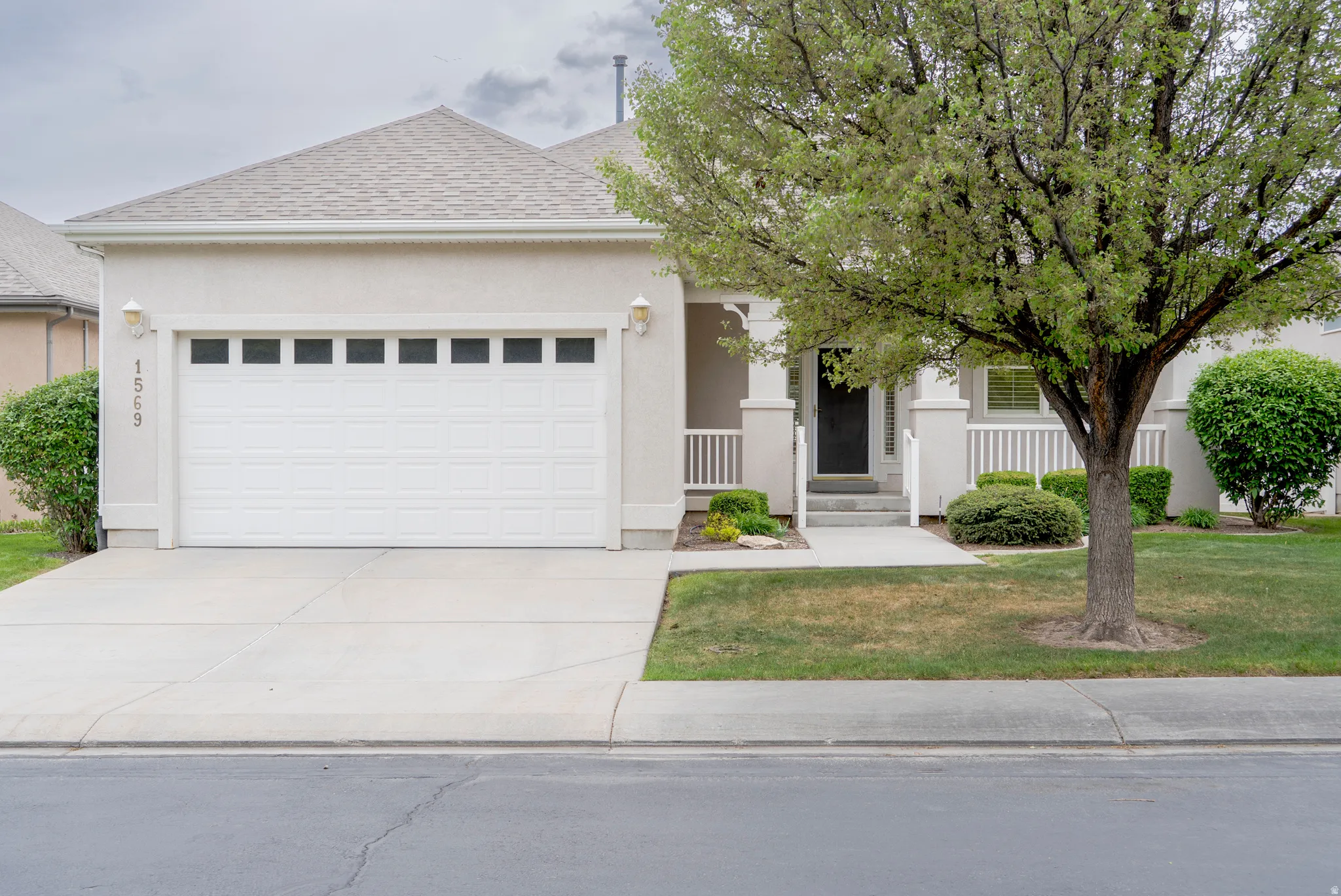 View of front facade with an attached garage, a front lawn, driveway, stucco siding, and a shingled roof