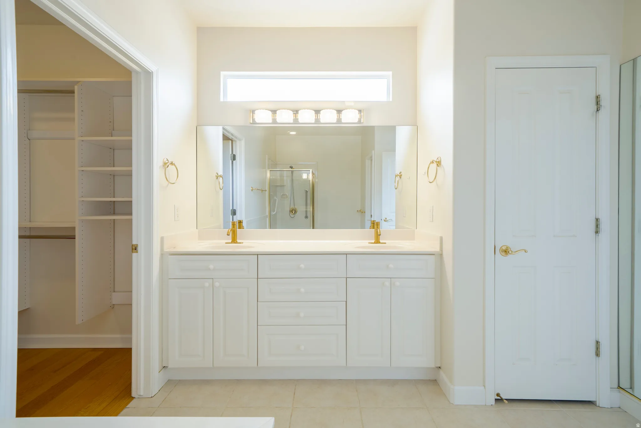 Full bath featuring double vanity, a spacious closet, light tile patterned floors, and a stall shower