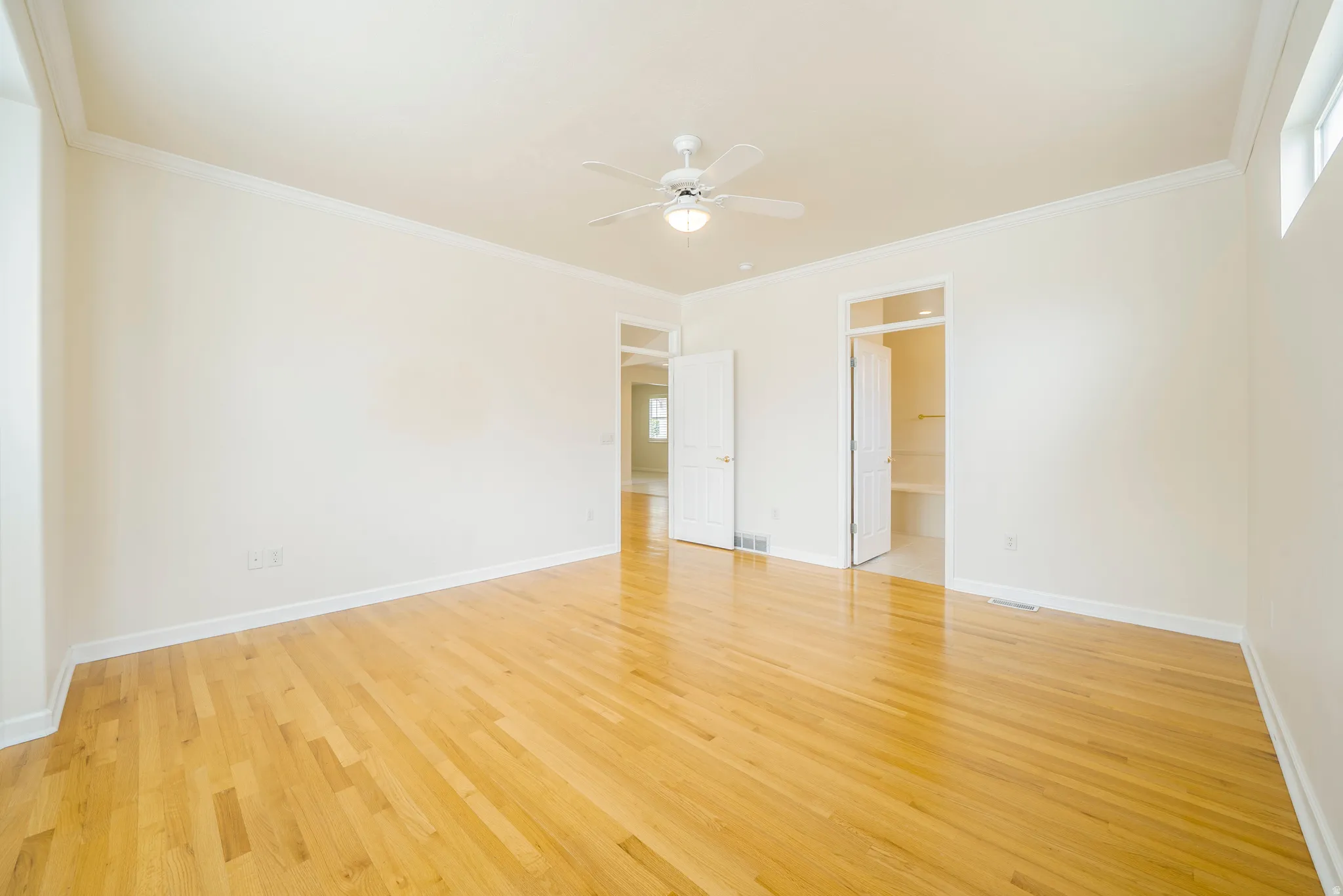 Unfurnished bedroom featuring light wood finished floors, ceiling fan, ensuite bathroom, and ornamental molding