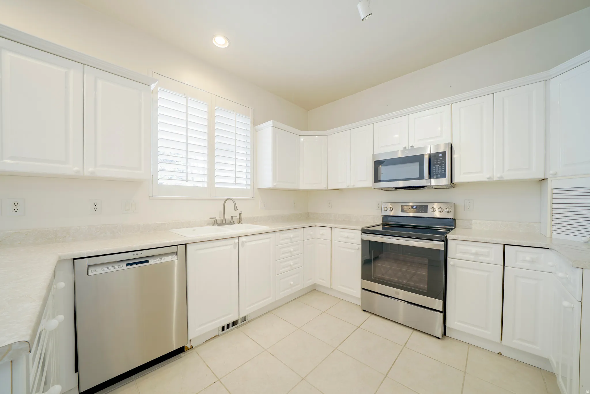 Kitchen with stainless steel appliances, white cabinets, light tile patterned floors, light stone counters, and recessed lighting