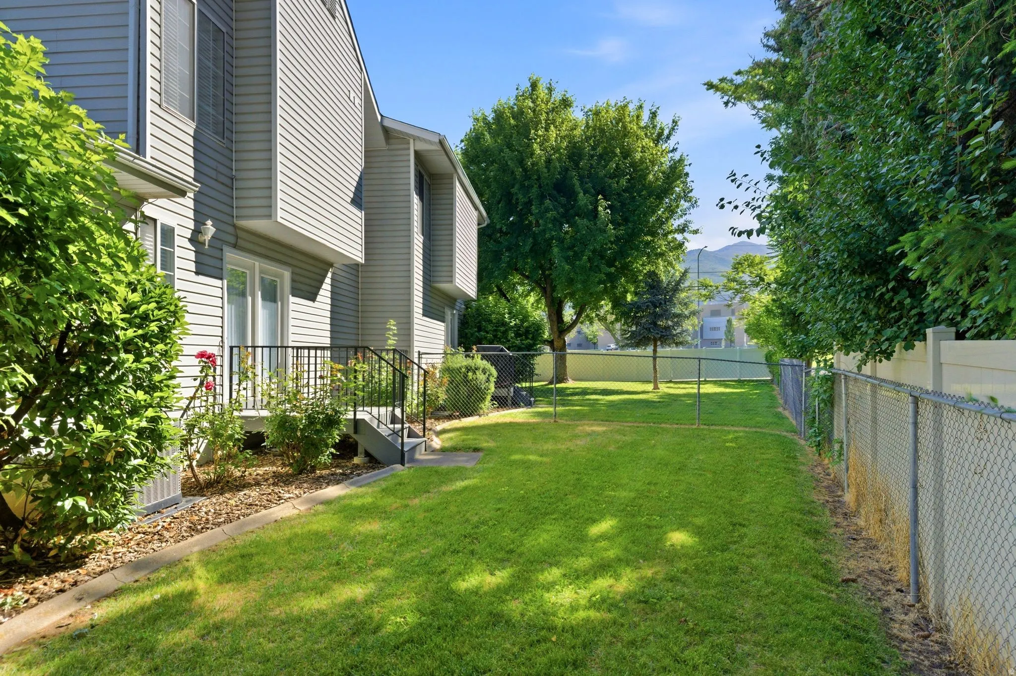 Spacious backyard featuring a chain-link fence, mature trees, and a manicured lawn