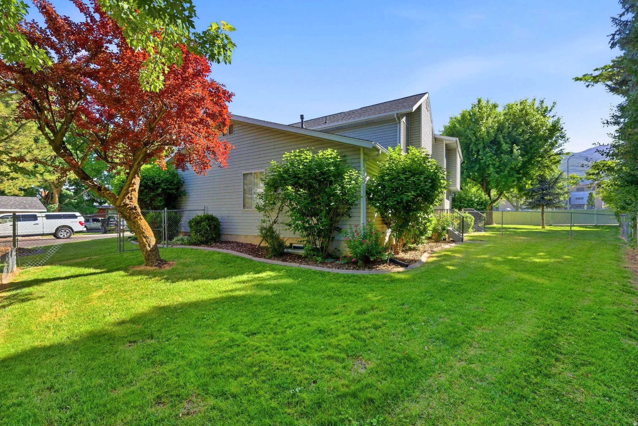 Spacious lawn area with mature trees, shrubbery, and a chain-link fence