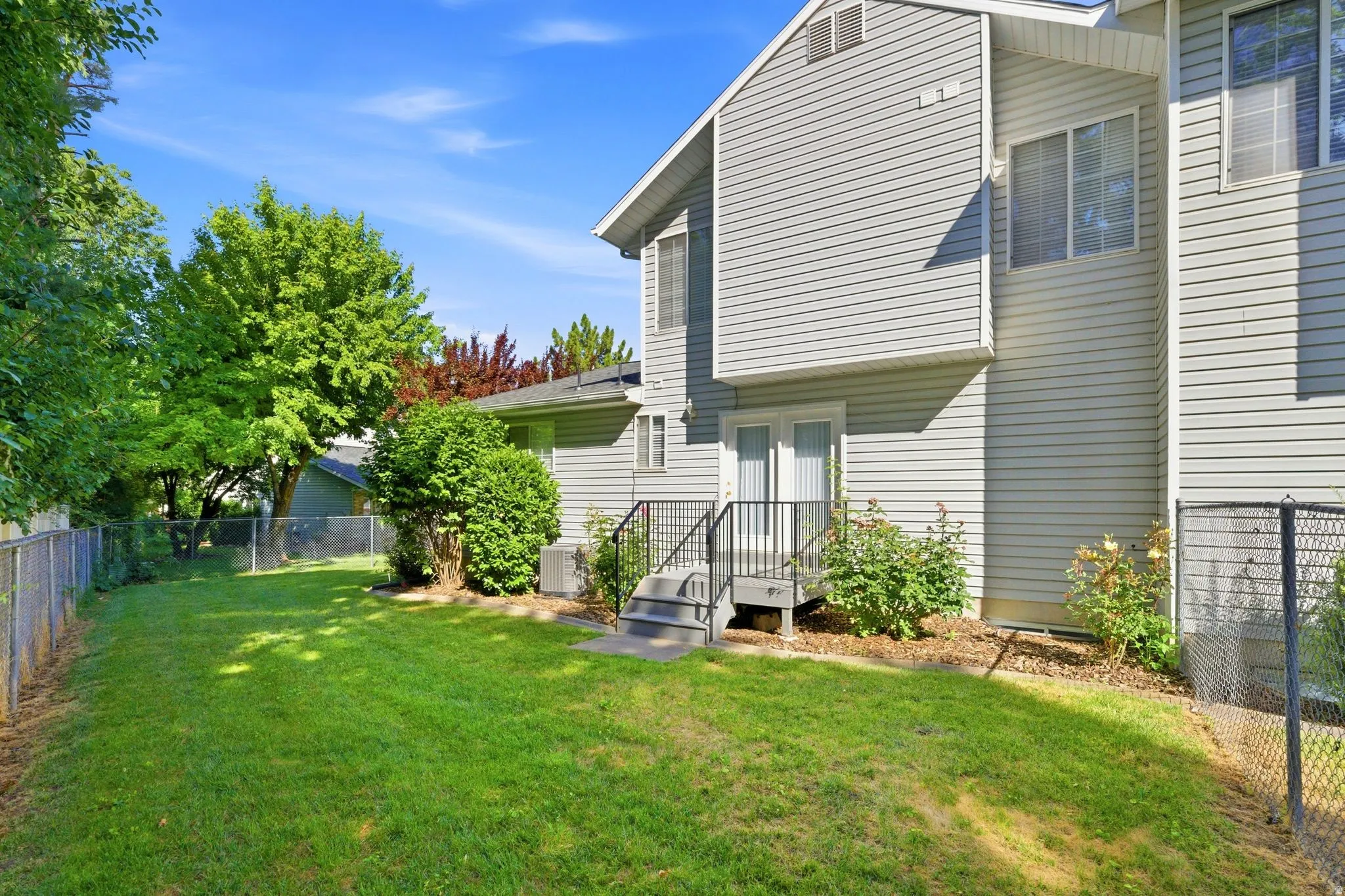 Rear exterior featuring light gray siding, a grass lawn, and mature perimeter trees