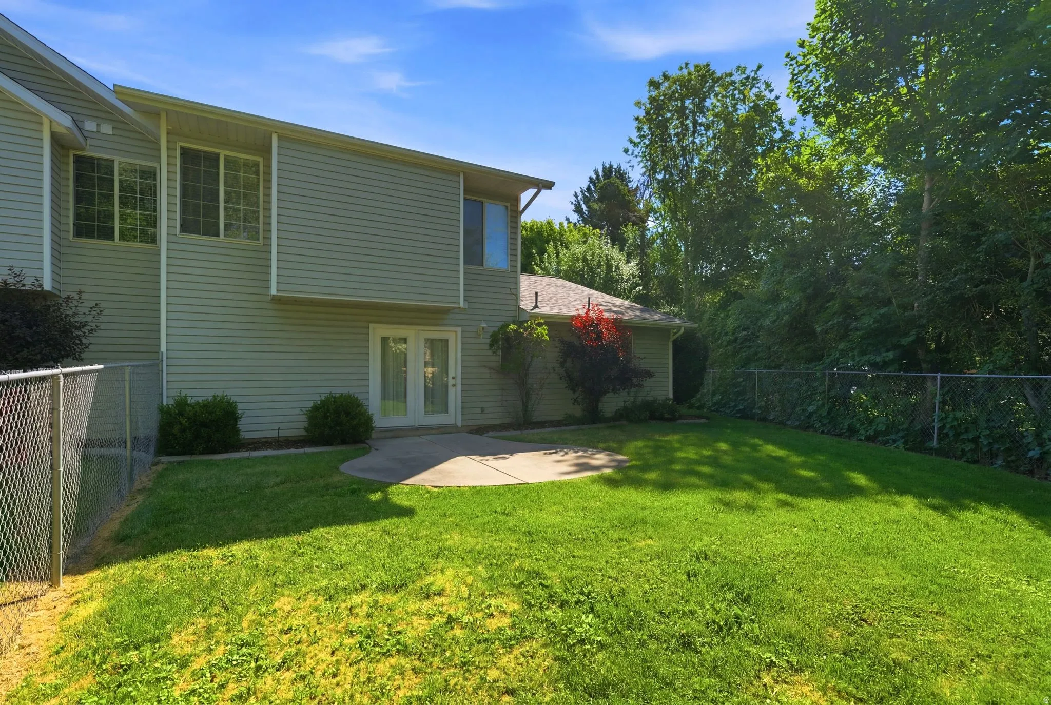 Expansive lawn area featuring a concrete patio, double glass doors, and mature perimeter trees
