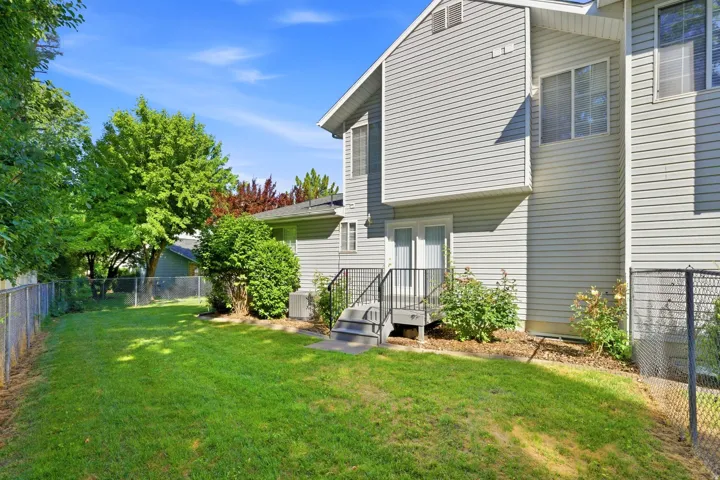 Rear exterior featuring light gray siding, a grass lawn, and mature perimeter trees
