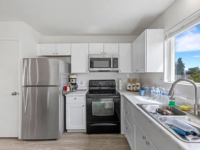 Kitchen featuring stainless steel appliances, light countertops, white cabinetry, light wood-type flooring, and tasteful backsplash