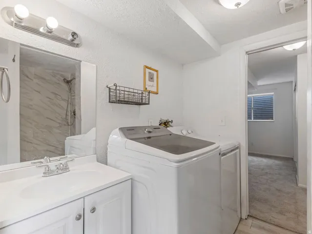 Laundry area with a textured ceiling, washer and clothes dryer, light wood-style flooring, and light carpet
