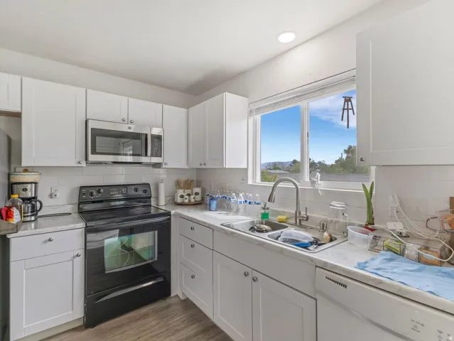 Kitchen featuring black range with electric stovetop, stainless steel microwave, white cabinets, and dishwasher