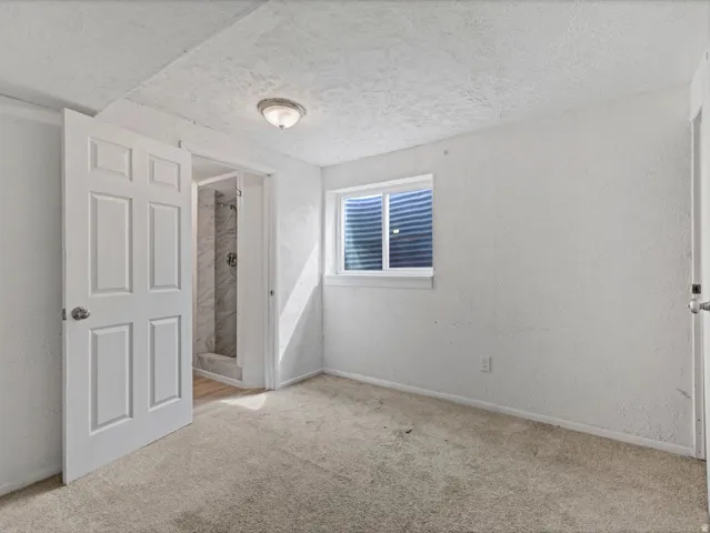 Unfurnished bedroom featuring a textured wall, a textured ceiling, carpet flooring, and ensuite bath