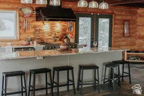 Kitchen featuring rustic walls, ventilation hood, a kitchen breakfast bar, light stone counters, and beam ceiling