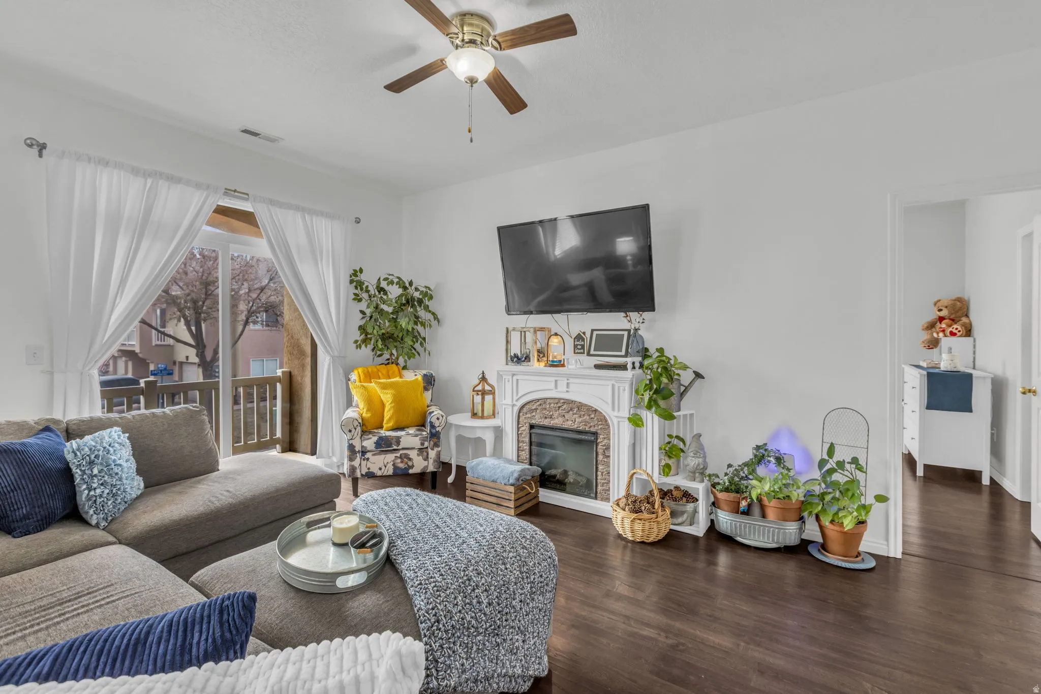 Living area featuring a ceiling fan, dark wood-style flooring, and a glass covered fireplace