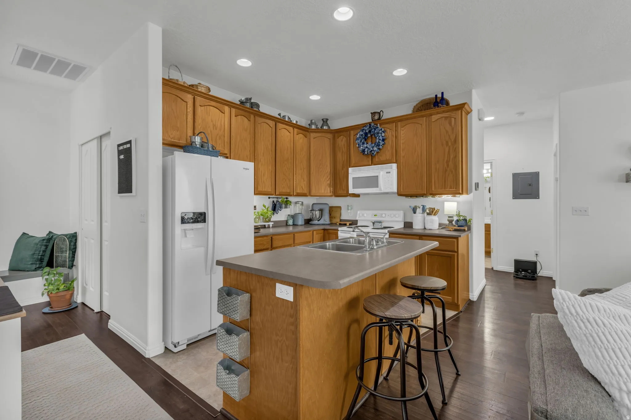 Kitchen featuring white appliances, dark wood-style floors, a center island with sink, wood finish cabinetry, and a breakfast bar area
