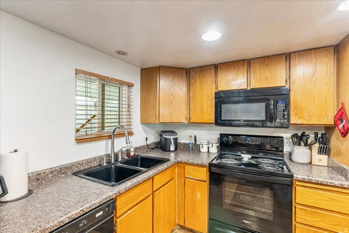 Kitchen featuring black appliances, wood finish cabinetry, dark countertops, and recessed lighting