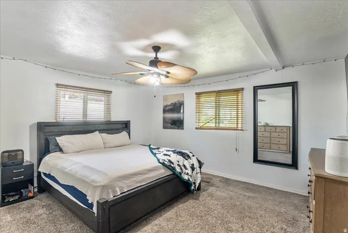 Bedroom featuring a textured ceiling, carpet floors, ceiling fan, and beamed ceiling