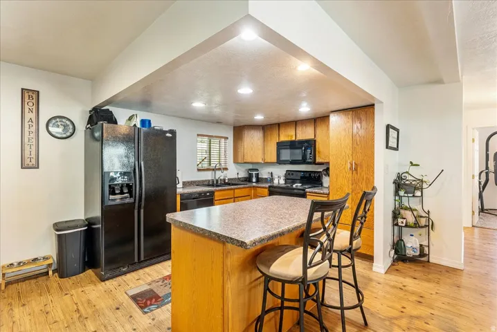 Kitchen featuring a breakfast bar area, black appliances, a center island, light wood finished floors, and recessed lighting