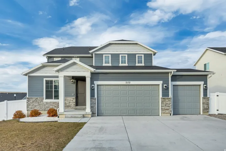 View of front of home with stone siding, driveway, roof with shingles, and an attached garage