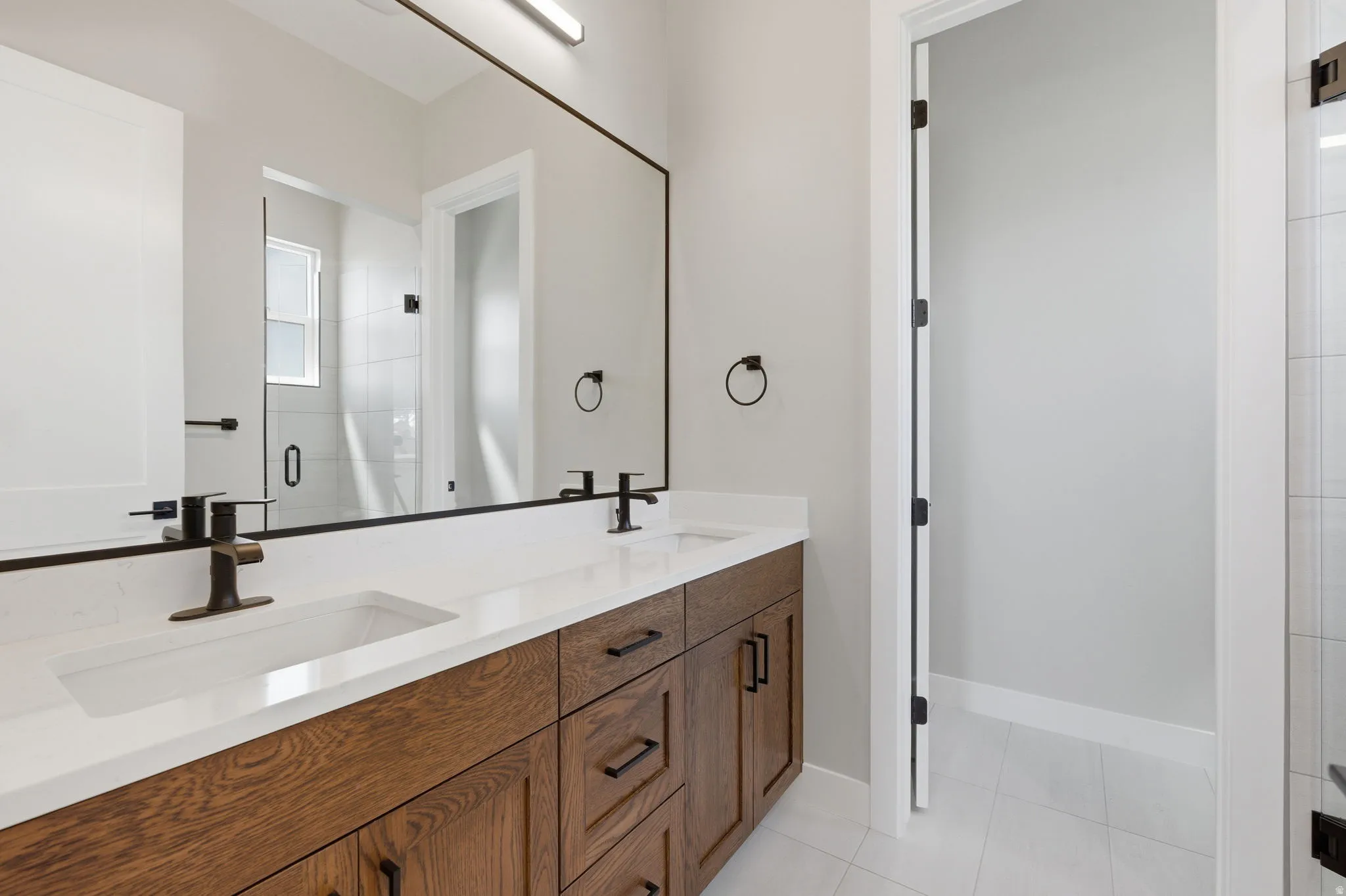 Bathroom featuring double vanity, light tile patterned floors, and a stall shower