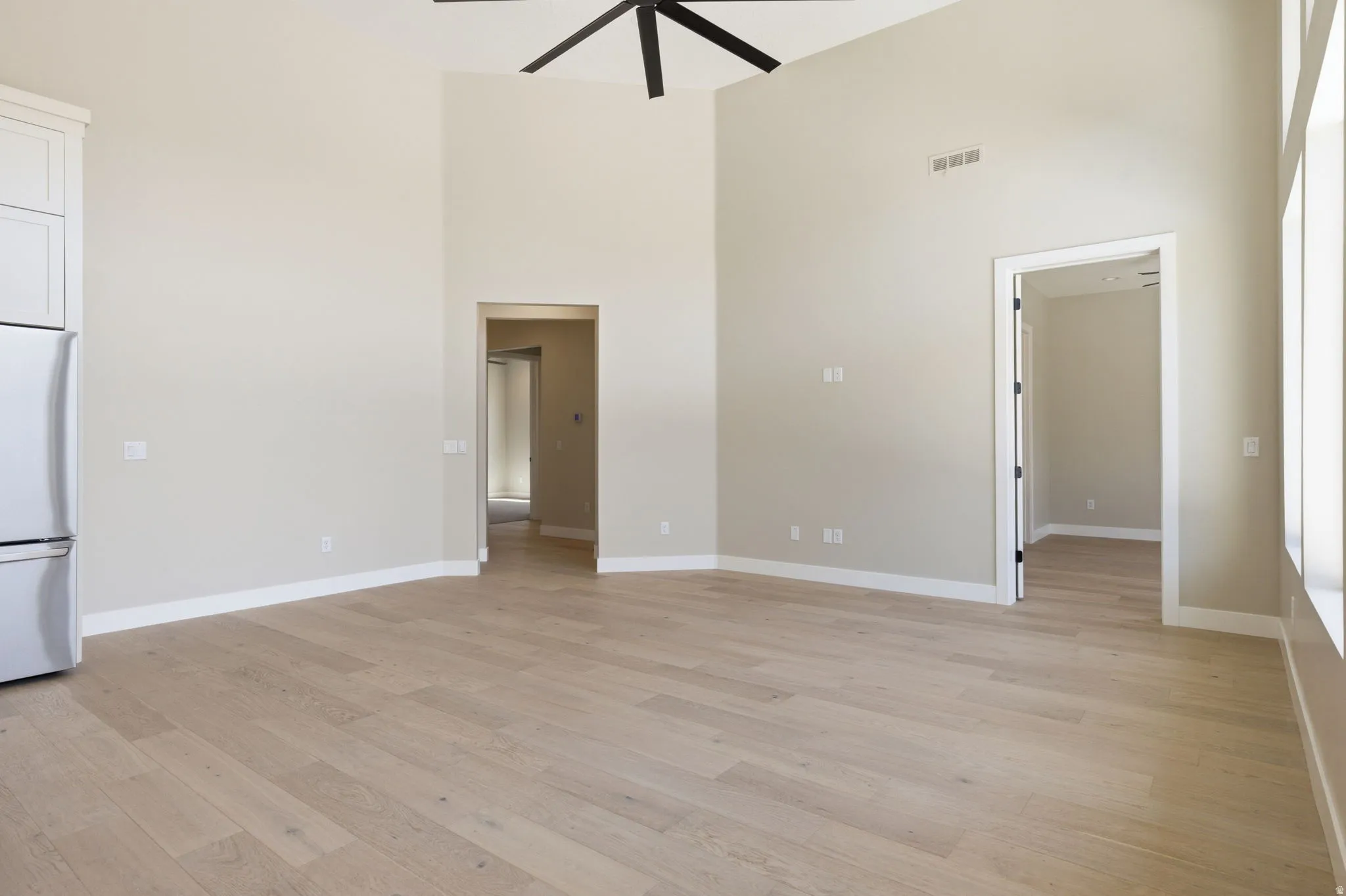 Unfurnished living room with ceiling fan, a high ceiling, and light wood-style floors