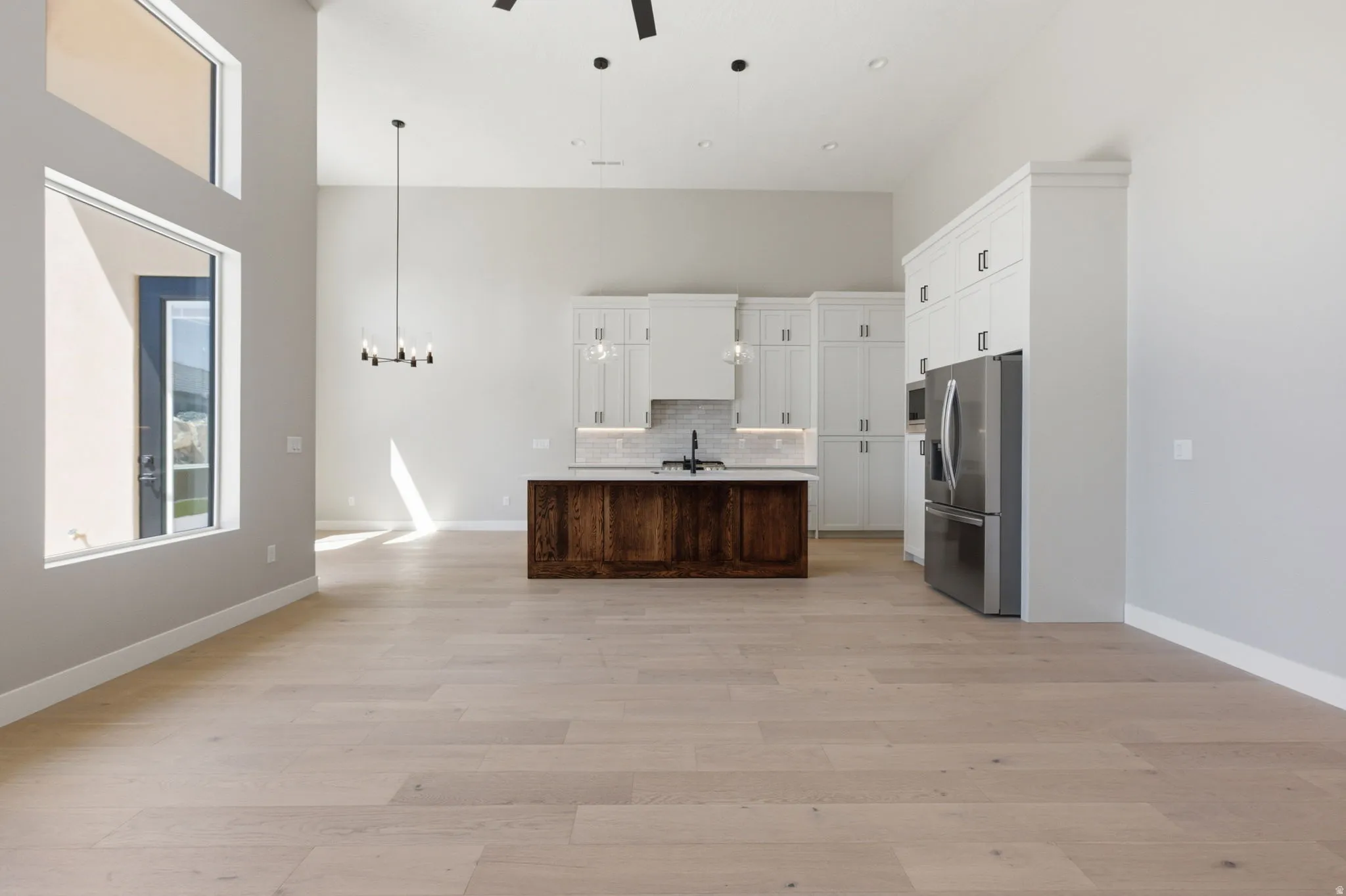 Two tone kitchen featuring healthy amount of natural light, open floor plan, ceiling fan, a center island with sink, and a high ceiling