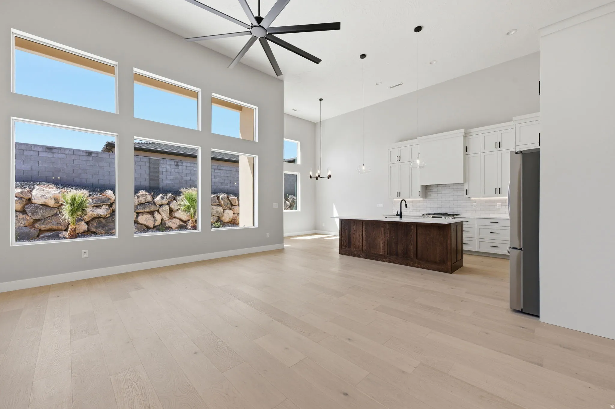 Dual tone kitchen featuring a high ceiling, a chandelier, a center island with sink, open floor plan, and freestanding refrigerator