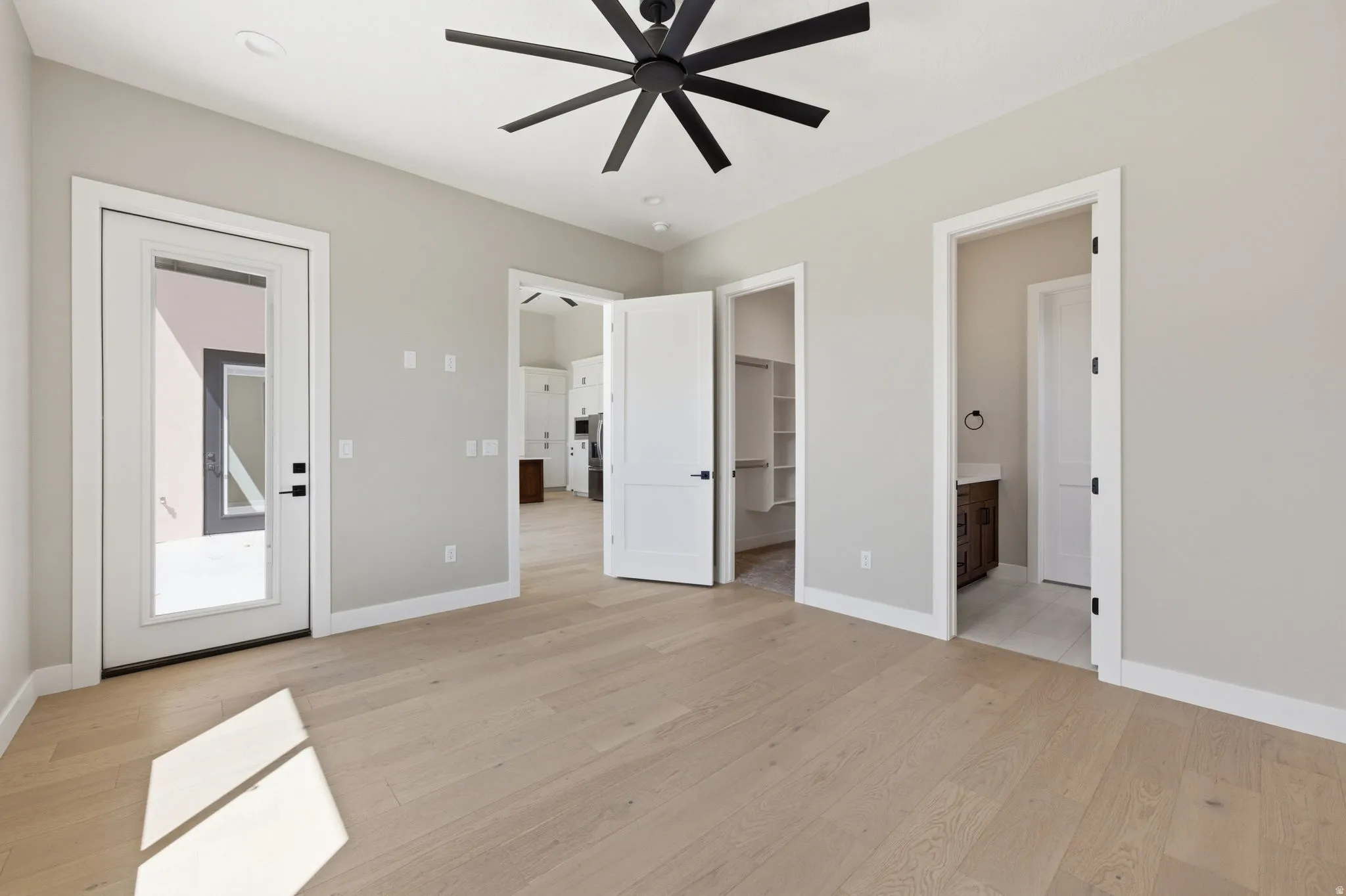 Unfurnished bedroom featuring light wood-style floors, a walk in closet, ceiling fan, and ensuite bath