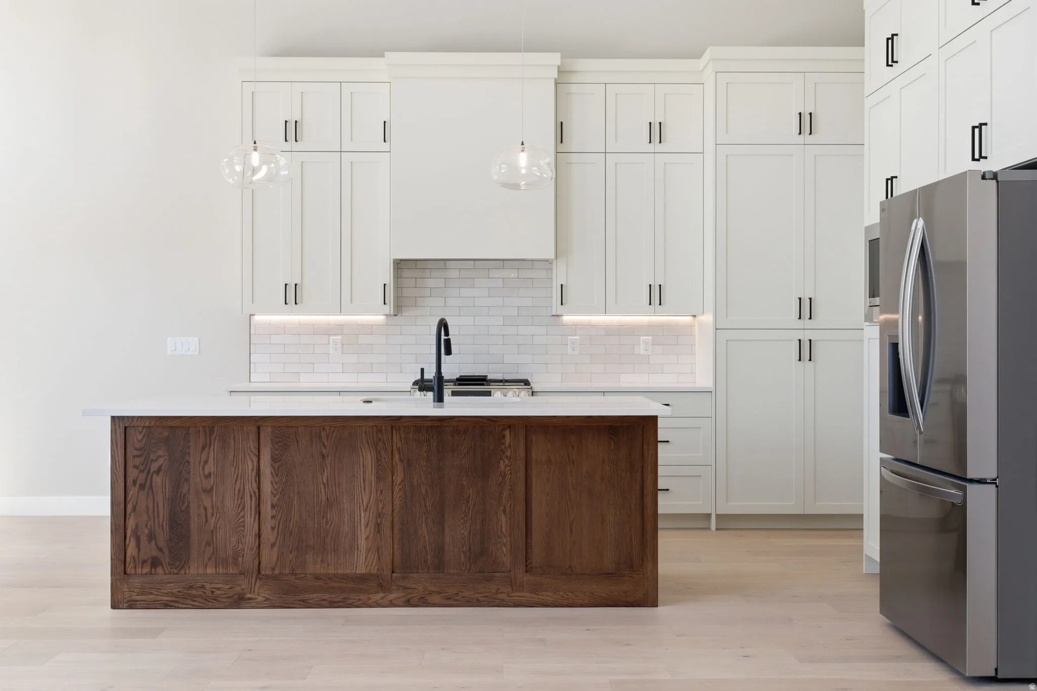 Two tone kitchen with stainless steel fridge with ice dispenser, a center island with sink, light wood-style floors, light stone counters, and dual tone cabinets