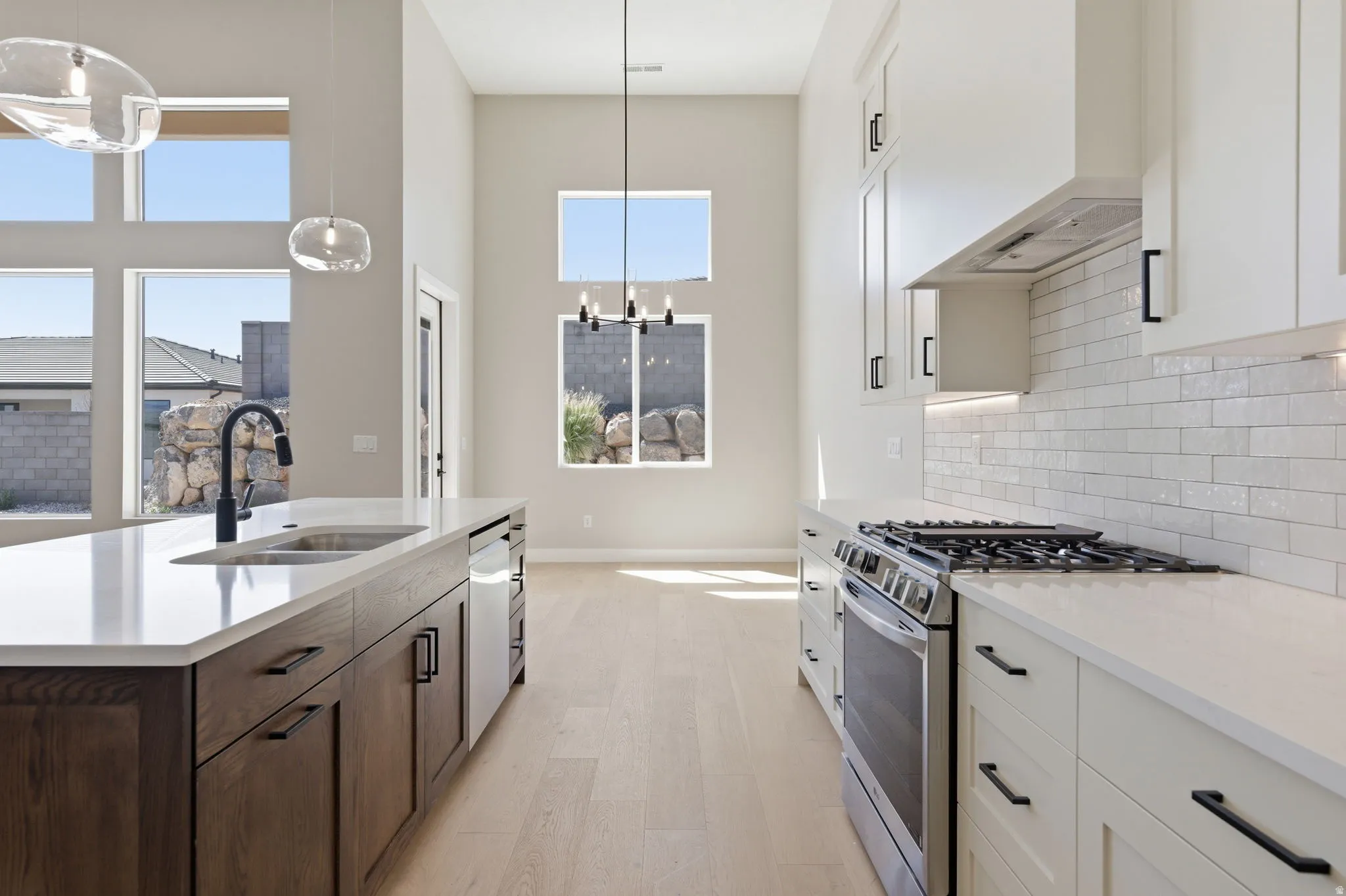 Two tone kitchen with stainless steel range with gas cooktop, light stone counters, light wood-style flooring, a center island with sink, and a high ceiling