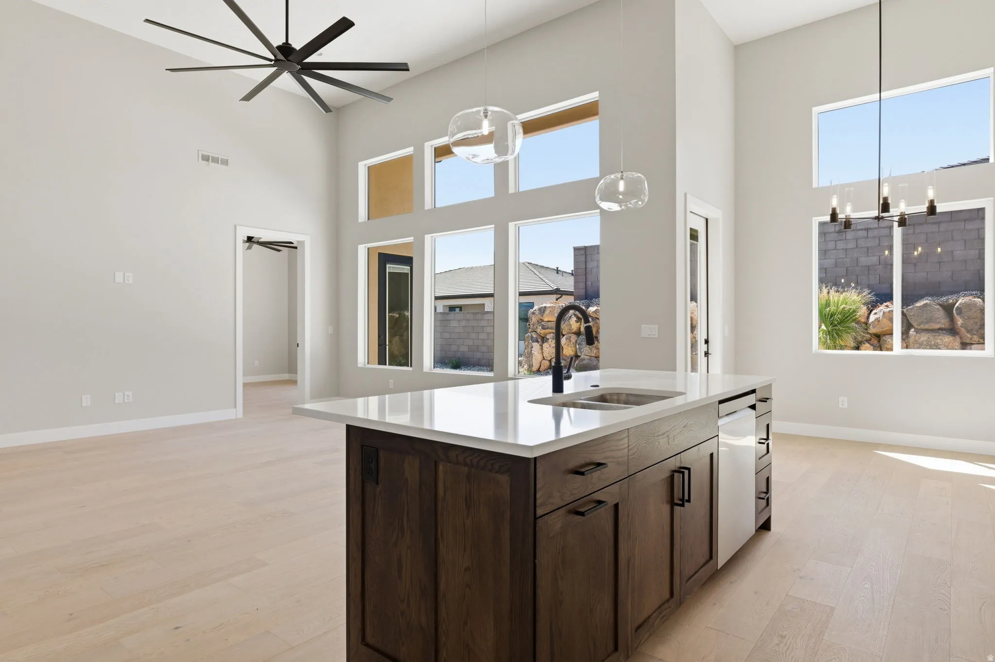 Kitchen with dark wood finish cabinets, a high ceiling, light wood-type flooring, hanging lights, and plenty of natural light