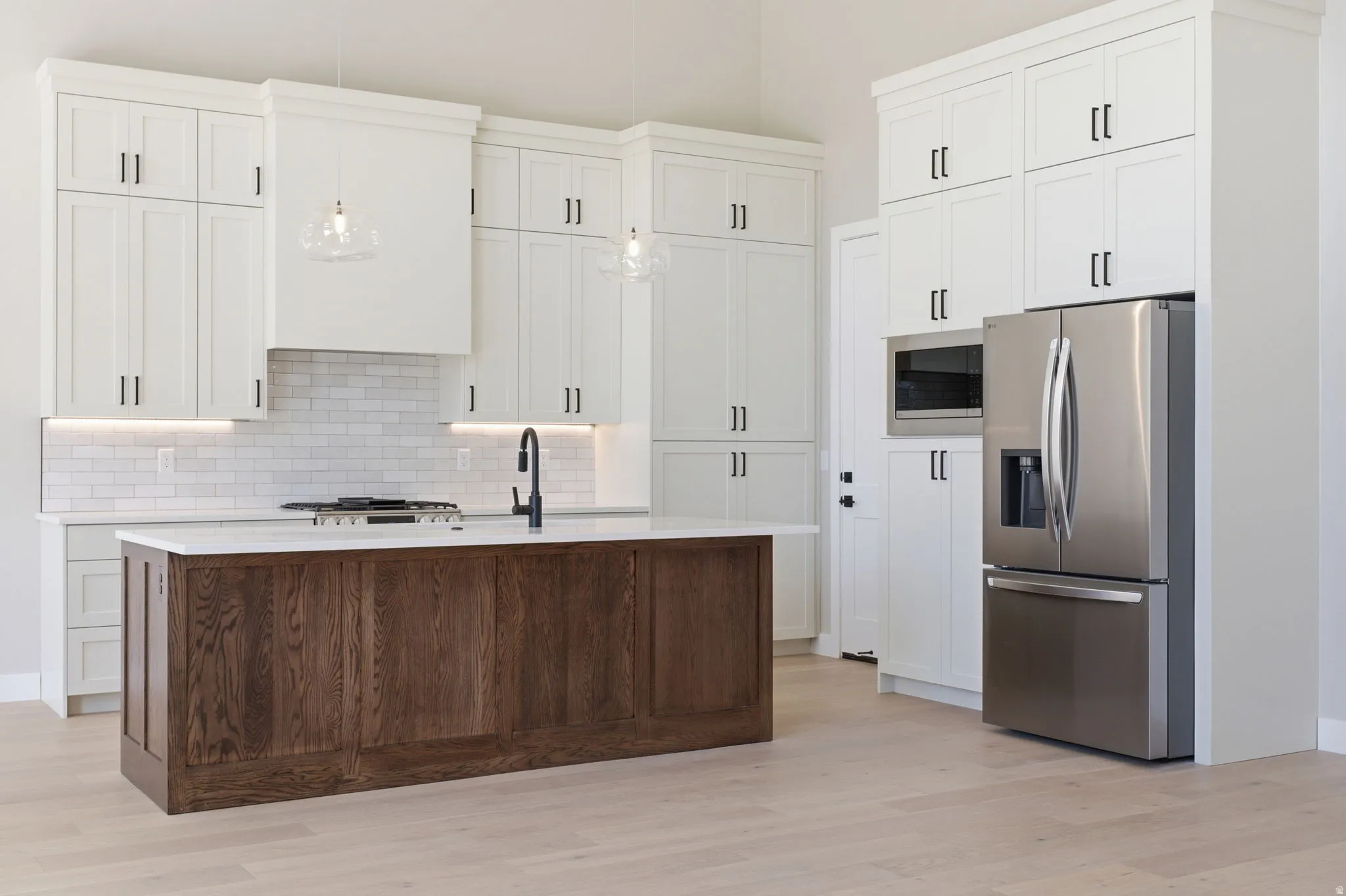 Two tone kitchen featuring stainless steel appliances, a center island with sink, light wood-type flooring, decorative light fixtures, and backsplash