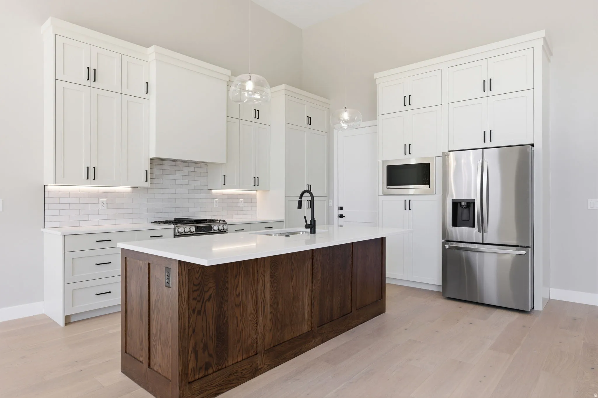 Two tone kitchen with stainless steel appliances, dual tone cabinets, light wood-style flooring, a kitchen island with sink, and decorative light fixtures