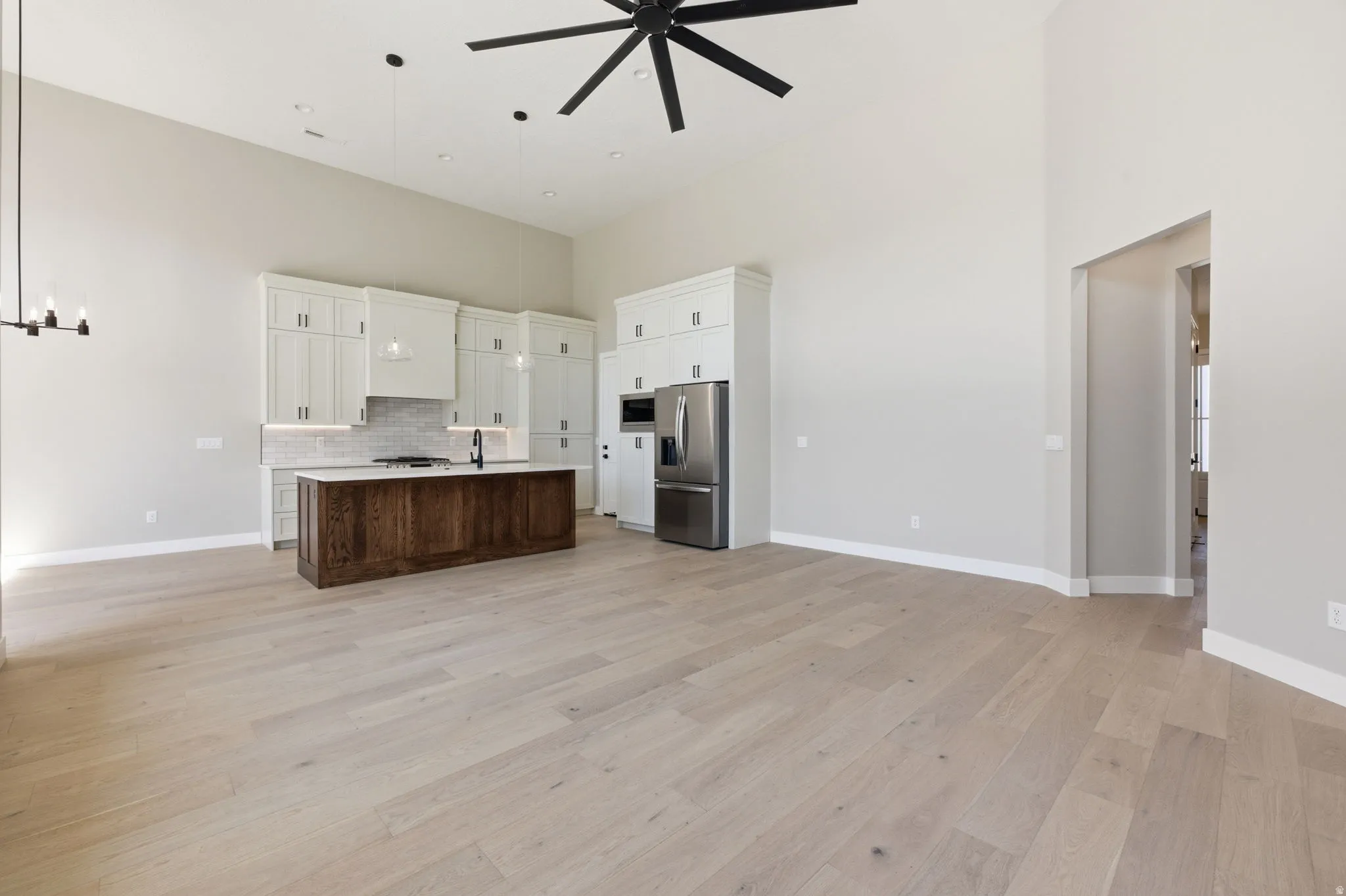 Two tone kitchen with open floor plan, stainless steel appliances, a high ceiling, ceiling fan, and light wood-style flooring