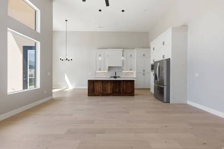 Two tone kitchen featuring healthy amount of natural light, open floor plan, ceiling fan, a center island with sink, and a high ceiling